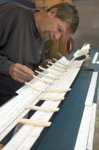 Papmodellen bygges gradvist op. Plankerne sættes sammen med nåle der placeres i sømhullerne. Når spanterne kommer på plads, kan man begynde at se skrogets form. 